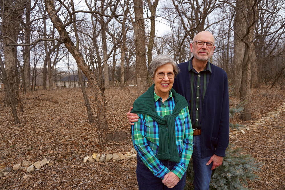Bob and Paige Wharram stand outside in front of a grove of trees in winter.