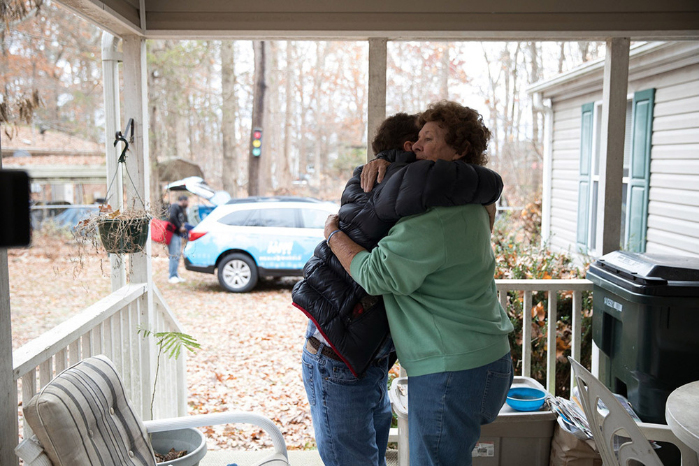 A person delivering food hugs a client receiving a home meal.